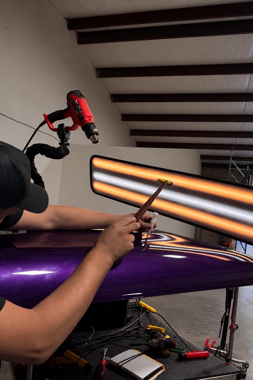 Technician performing paintless dent repair with inspection light on a purple vehicle
