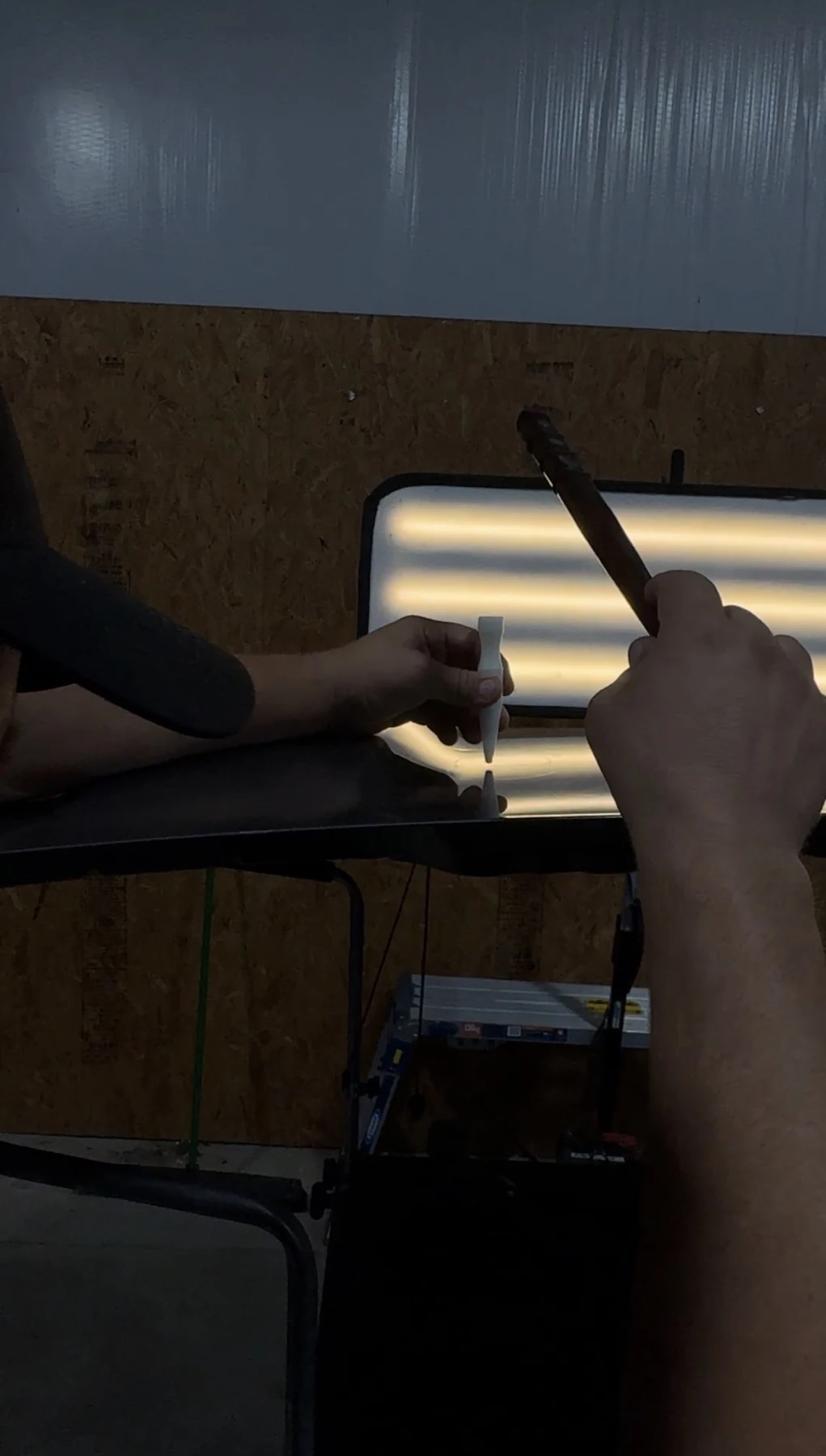 Actual paintless dent repair technician hands using precision tools with an illuminated reflection board
